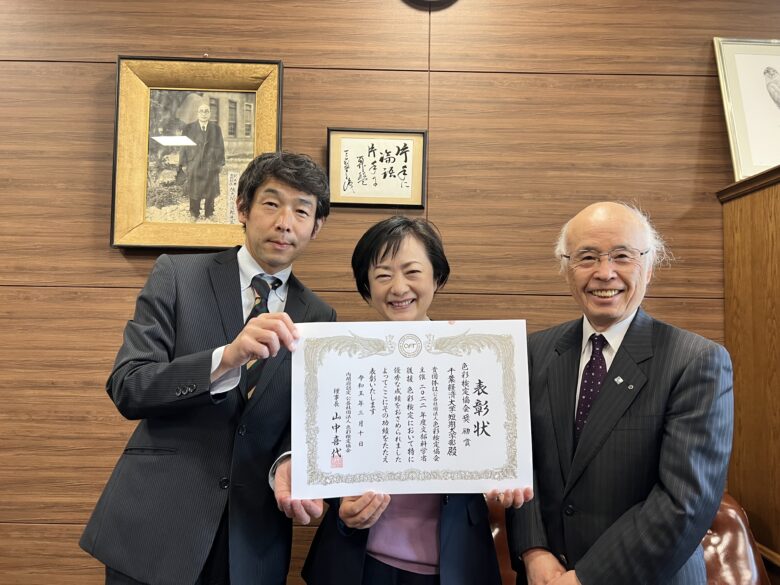 本学に来校された色彩検定協会 吉野勝さん（写真左）。本学の佐久間勝彦学長と色彩学の授業を担当する沢谷有梨准教授に賞状が手渡されました。