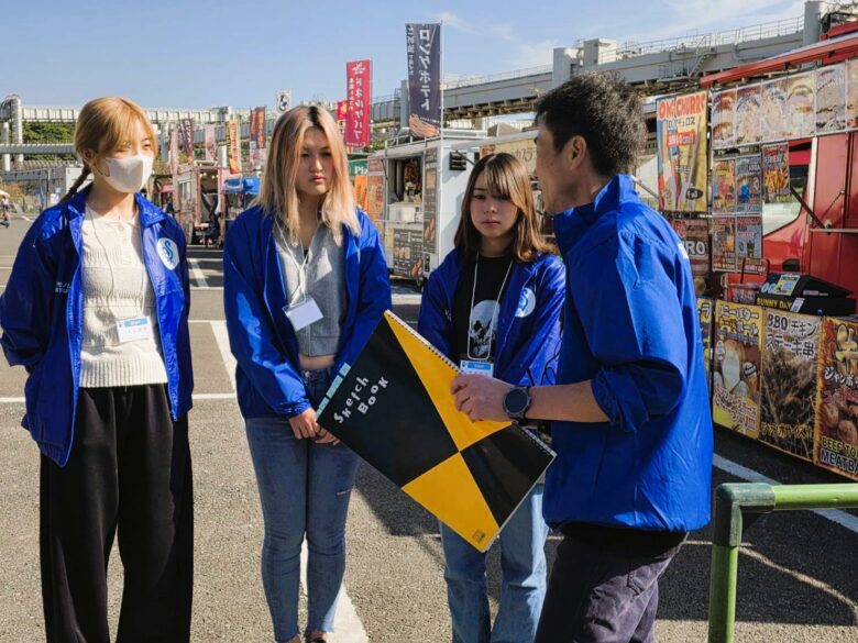 モノレールの車両と同色のスタッフジャンパーを身にまとった学生たち。打ち合わせ中の一コマ。